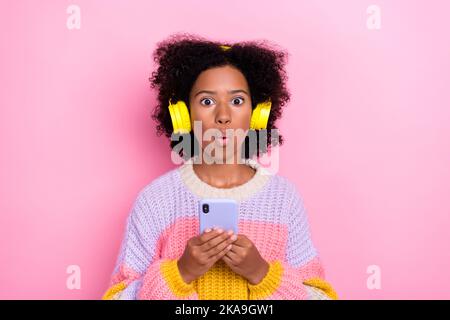 Portrait von stauned beeindruckt Mädchen gewellte Frisur Sweatshirt Kopfhörer halten Smartphone zuhören Wiedergabeliste auf rosa Hintergrund isoliert Stockfoto