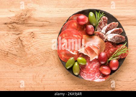 Traditionelle italienische Antipasti. Wurstplatte mit verschiedenen Wurstsorten - Salami, bresaola, proscuitto serviert mit Oliven auf Holztisch. B Stockfoto