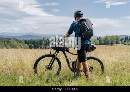 Bikepacking in den Bergen. Mann, der mit seinem Fahrrad und Rucksack auf einer Wiese steht, bereit für eine Bikepacking-Abenteuerfahrt. Stockfoto