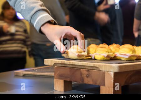 Hand einer Person, die während einer Firmenveranstaltung ein Mini-Sandwich auf einem Buffettisch nimmt Stockfoto