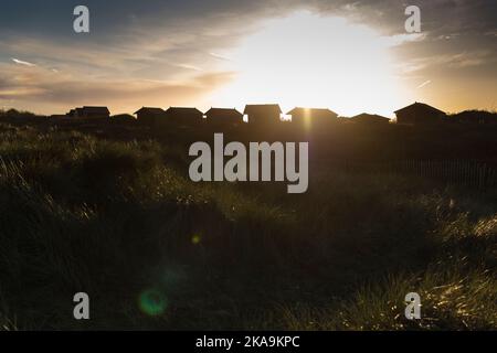 Sonnenuntergang mit einer Reihe von Strandhütten in der Ferne, die gegen den Abendhimmel im Vordergrund geschildet wurden Stockfoto