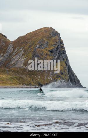 Surfer auf einer Welle mit Berg im Hintergrund in Unstad Lofoten Norwegen Stockfoto