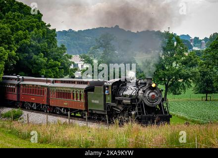 Ronks, Pennsylvania, 18. Juni 2021 - Blick auf einen restaurierten Dampfzug, der sich an einem Sommertag mit Rauch und Dampf aus dem Wald nähert Stockfoto