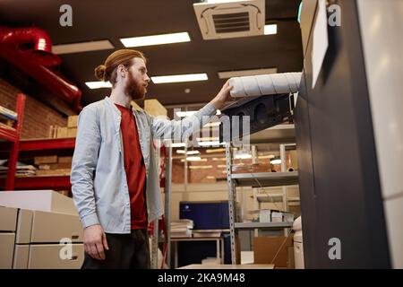 Seitenansicht Porträt eines jungen Mannes, der in der industriellen Druckerei Vinylrollen herausnimmt Stockfoto