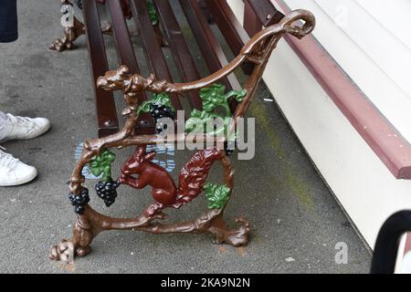 Kunstvoll bemalte Eisenarbeiten Ende einer Bank, die ein rotes Eichhörnchen zeigt, das Trauben in der Station in Ravenglass auf der schmalen Spur Ravenglass und Eskdale frisst Stockfoto