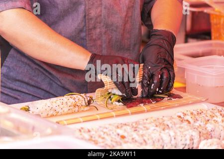 Der Küchenchef bereitet Sushi im Freien in der offenen Küche zu. Street Food Festival. Stockfoto