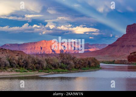 Ein antirepuskulärer Strahl über Fisher Towers & Waring Mesa und dem Colorado River, von der Red Cliffs Ranch bei Sonnenuntergang. Moab, Utah. Stockfoto