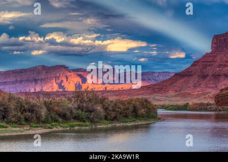 Ein antirepuskulärer Strahl über Fisher Towers & Waring Mesa und dem Colorado River, von der Red Cliffs Ranch bei Sonnenuntergang. Moab, Utah. Stockfoto