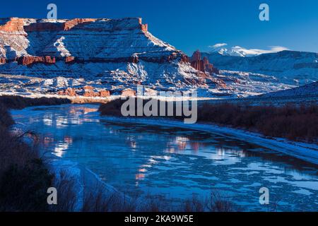 Fisher Towers über dem eisigen Colorado River bei Sonnenuntergang im Winter mit den La Sal Mountains dahinter. In Der Nähe Von Moab, Utah. Stockfoto