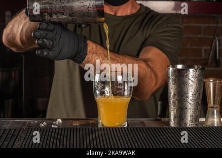 Der Barkeeper in der Bar goss einen alkoholischen Cocktail in ein Glas. Sommer Party Hintergrund. Stockfoto