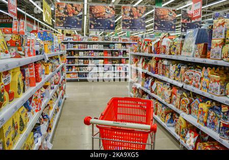 Moskau, Russland, November 2019: Roter Korb, Supermarktwagen zwischen den Reihen im Supermarkt mit Weihnachtsgebäck für Kinder: Schokoladenfigur Stockfoto