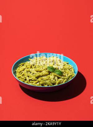 Klassische italienische Pasta, Trofie al Pesto minimalistisch auf einem roten Tisch. Pasta mit Pesto-Sauce und Parmesankäse auf einem farbenfrohen Hintergrund. Stockfoto
