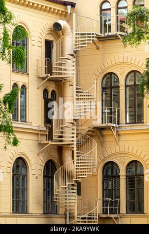 Nykoping, Schweden - 13. Juni 2022: Architektonische Details in der Nahaufnahme einer Metallspiraltreppe, die nach der gelben Außenwand führt, machen das traditionelle Jahr 1 wieder wetterlich Stockfoto