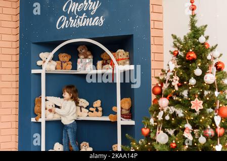 Ein kleines Mädchen wählt in einem Weihnachtsgeschäft Teddybären aus. Weihnachtskarte. Stockfoto