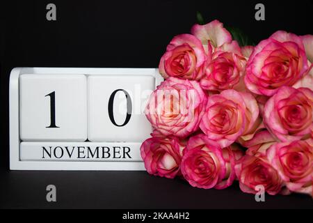 November 10 Holzkalender, weiß auf schwarzem Grund, rosa Rosen liegen in der Nähe. Stockfoto