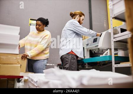 Seitenansicht von zwei Arbeitern, die im Laden eine industrielle Druckmaschine betreiben Stockfoto