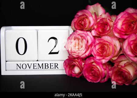 November 2 Holzkalender, weiß auf schwarzem Grund, rosa Rosen liegen in der Nähe. Stockfoto
