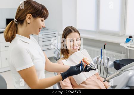 Lächelnder Zahnarzt demonstriert für Patienten Nachbau der menschlichen Kiefer und erklärt Karies Prävention und Behandlung. Zahnmodell in den Händen des Arztes. Konzeptfoto Stockfoto