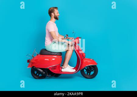 Foto in voller Größe von schönen jungen Kerl fahren Motorrad persönlichen Transport gekleidet stilvolle rosa Blick isoliert auf aquamarinfarbenem Hintergrund Stockfoto