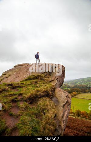 Mann, der auf dem Felsen steht, rast den Hanging Stone in der Landschaft von Ceshire bei Danebridge Ceshire aus Stockfoto