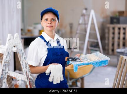 Frau Baumeister hält Farbe Walze und Tablett, Hausverbesserung arbeitet Stockfoto