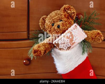 Brauner Teddybär in roten Santa Claus Socken. Plüschtier mit Weihnachtsgeschenk. Neujahrsgeschenk in hellem goldenem Papier. Stockfoto