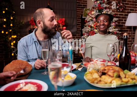 Pärchen essen, Sekt trinken am festlichen weihnachtstisch, feiern Urlaub mit der Familie. Mann und Frau genießen hausgemachte Weihnachtsgerichte zu Hause Party mit Freunden Stockfoto