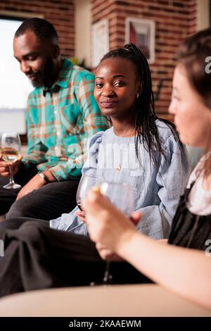 Glücklich lächelnd junge Erwachsene afroamerikanische Frau vertikale Nahaufnahme genießen soziales Leben, trinken Wein bei Freunden, Partner Wohnung, zu Hause, Haus gemacht Party, Wiedervereinigung, Sammeln. Stockfoto