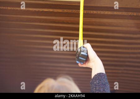 Unschärfe-Frau Bauarbeiter misst Gipskartondecke mit Maßband. Weibliche Hände, die Fenstermessungen vornehmen. Nicht fokussiert. Stockfoto