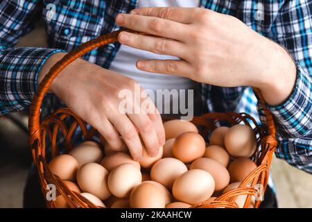 Defokussieren Mann Hand hält Drahtkorb mit frischen Hühnereiern. Nahaufnahme der männlichen Hände, die Eier im Korb zeigen. Weibliche Hände halten rohe Eier in Korb, Closeus Stockfoto