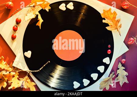 Vintage Vinyl Schallplatten in Papierärmel auf schwarzem Hintergrund und Papierärmel. Gelbe Eichenblätter auf orangefarbenem, magentafarbenem Papierhintergrund mit Herbstfärbung Stockfoto