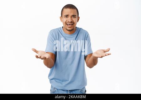 Frustrierter Mann schüttelt die Hände, sieht verwirrt und verärgert aus und fragt, warum, über weißem Hintergrund stehend Stockfoto