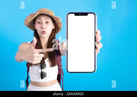 Glückliche asiatische Frau Reisende mit einer Tasche und zeigen einen Finger, während ein weißer leerer Bildschirm des Mobiltelefons auf blauem Hintergrund, Tourist Asia Mädchen mit einem Reise-Promotion-Angebot. Stockfoto