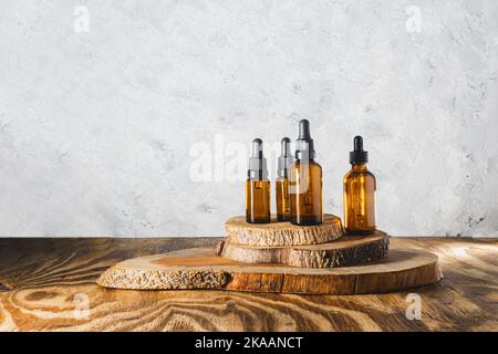 Stillleben von Flaschen ätherischer Öle auf Treibholz auf grauem texturiertem Hintergrund. Hintergrund mit Kopierbereich Stockfoto