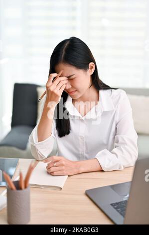 Porträt, betonte junge asiatische Geschäftsfrau besorgt über die Frist ihres Projekts, leiden unter Kopfschmerzen oder Augen Belastung während der Arbeit im Büro. Stockfoto