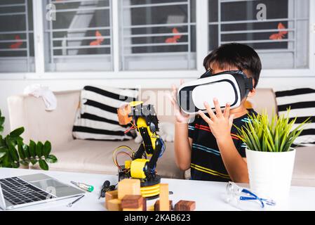 Asiatischer Junge mit VR-Brille auf Roboterarm in der Werkstatt Stockfoto