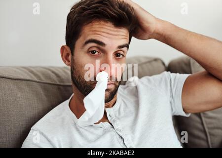 Sieht wieder wie seine Grippesaison aus. Beschnittenes Porträt eines jungen Mannes mit einem Gewebe in der Nase aufgrund von Nasennebenproblemen. Stockfoto