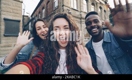 Sichtbild von aufgeregten männlichen und weiblichen Reisenden, die im Freien Online-Videoanruf mit Gadget führen, die Kamera betrachten und über die schöne Stadt um sie herum sprechen. Stockfoto