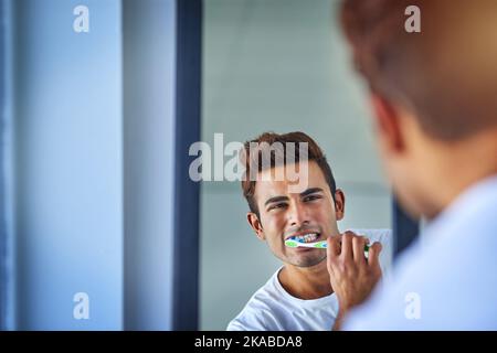 Die Mundgesundheit zu einer Priorität zu machen. Porträt eines glücklichen jungen Mannes, der sich zu Hause die Zähne putzt. Stockfoto