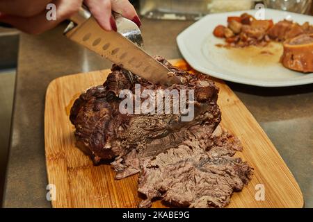 Der Koch schneidet Scheiben aus einem Stück lang gegartem Rindfleisch Stockfoto