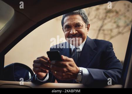 Ich gebe nie SMS, während ich fahre. Ein reifer Geschäftsmann benutzt ein Telefon, während er sich an sein Auto lehnt. Stockfoto