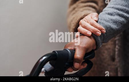 Krank gibt Ihnen immer eine helfende Hand. Eine unkenntliche ältere Frau hilft ihrem Mann, mit seinem Wanderer zu gehen. Stockfoto