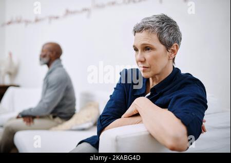 Ärger im Paradies. Ein unglückliches Seniorenpaar, das getrennt auf einer Couch sitzt, nachdem es zu Hause einen Streit geführt hat. Stockfoto