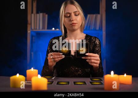 Wahrsagerin von Händen, die Tarot-Karten auf dem Tisch neben brennenden Kerzen im Kerzenlicht halten.Tarot-Karten verteilen sich auf dem Tisch. Prognosen Stockfoto