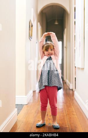 Ich bin eine Ballerina Prinzessin. Porträt eines fröhlichen kleinen Mädchens, das ihre Arme in die Luft streckt, während es zu Hause auf die Kamera schaut. Stockfoto