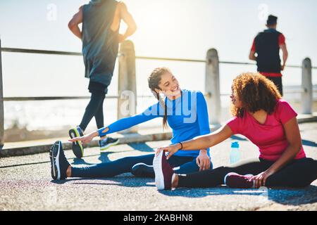 Workout Buddys sind eine gute Möglichkeit, die Motivation zu steigern. Zwei sportliche junge Frauen machen gemeinsam Aufwärmübungen im Freien. Stockfoto