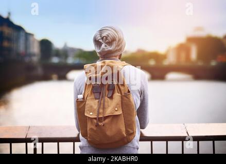 Es ist schwer zurückzublicken, wenn Sie so viel gesehen haben. Rückansicht eines jungen Mannes, der von einer Brücke aus den Blick auf die Stadt schaute. Stockfoto