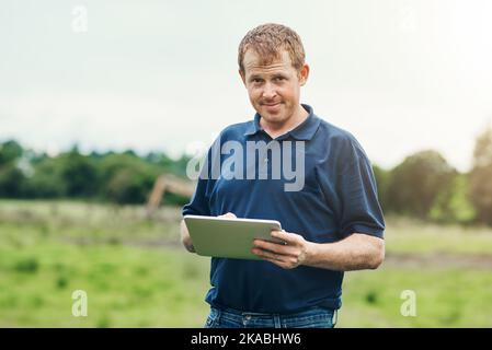 Sogar Landwirte haben Tabletten. Porträt eines fröhlichen jungen Bauern, der ein digitales Tablet hält, während er draußen auf seinem Land steht. Stockfoto