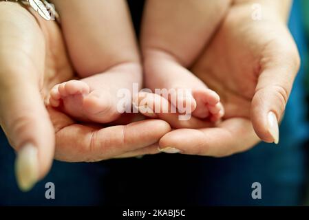 Kleine Füße, die große Fußabdrücke hinterlassen. Nahaufnahme einer Mutter, die ihre kleinen Füße in den Händen hält. Stockfoto