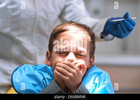 Ich will nicht, dass meine Zähne gezogen werden. Ein ängstlicher kleiner Junge, der sich auf einem Zahnarztstuhl legt und seinen Mund geschlossen hält, um den Zahnarzt von der Arbeit abzuhalten Stockfoto